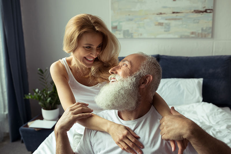 Älterer Mann lächelt blonde Frau im Schlafzimmer an