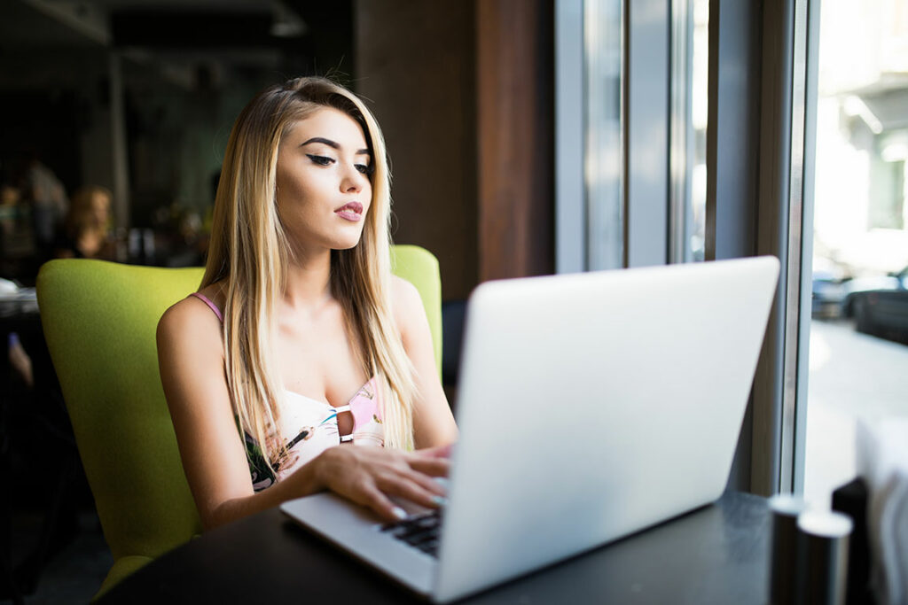 Junge blonde Frau sitzt im Cafe vor einem Laptop