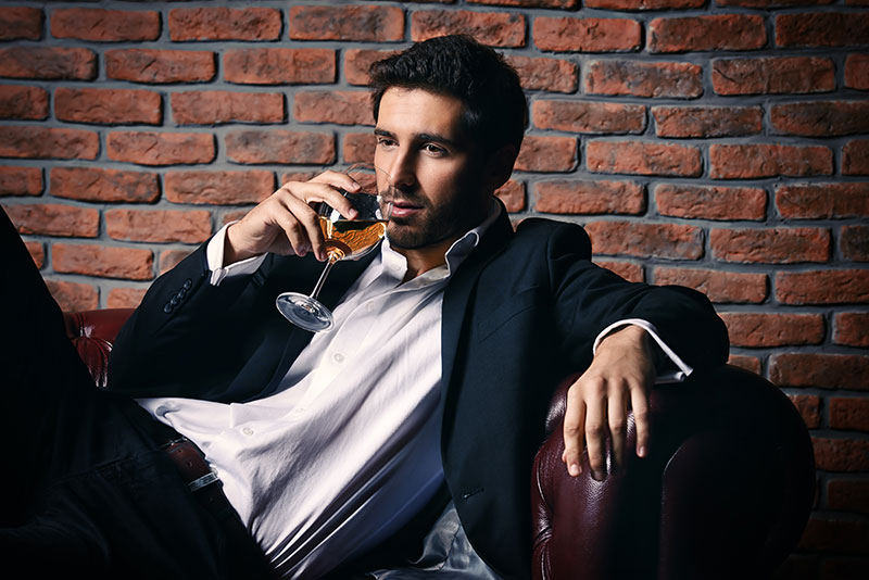 Mann sitzt in einem Sessel und trinkt ein Glas Wein