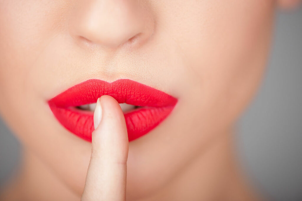 Nahaufnahme von weiblichen roten Lippen mit einem Finger vor dem Mund