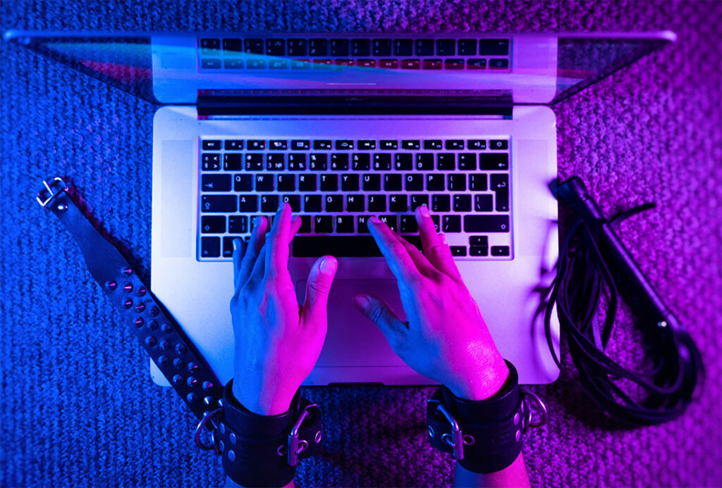 Hände mit BDSM-Handschellen tippt auf Laptop