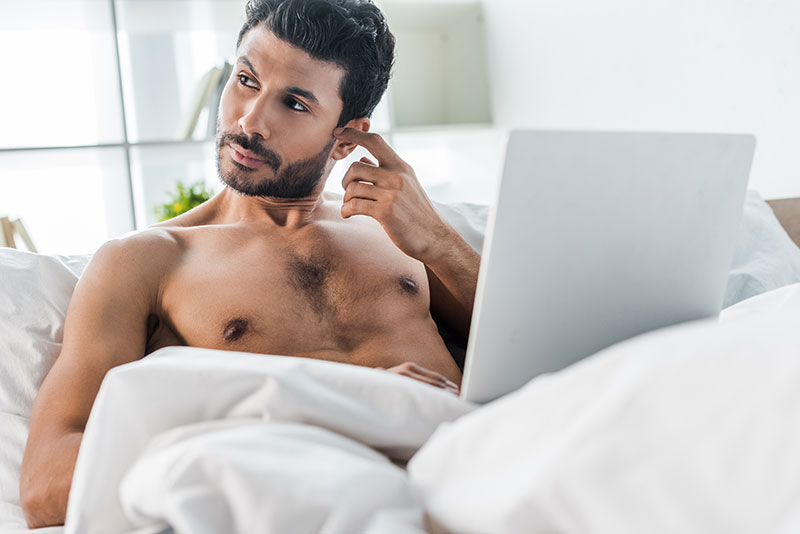 Nachdenklicher Mann mit Laptop im Bett