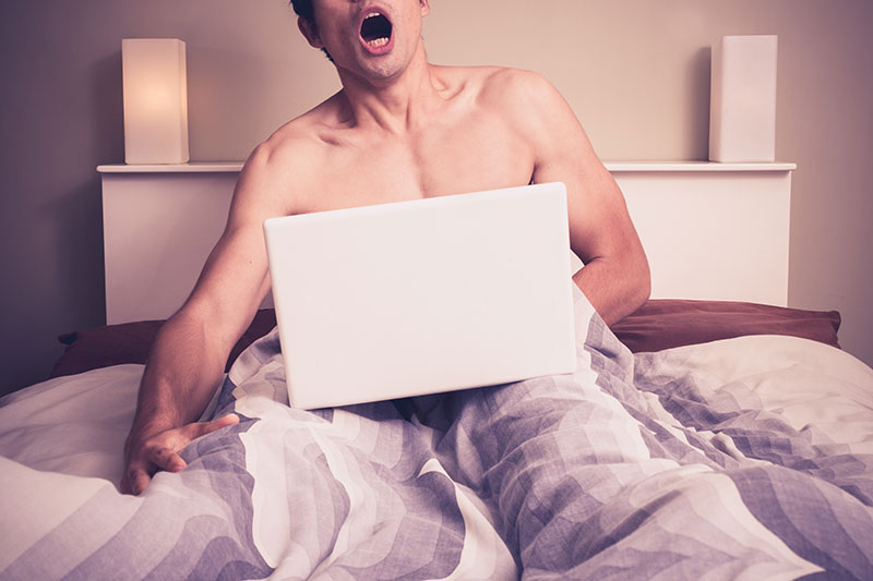 Mann stöhnt im Bett vor Laptop