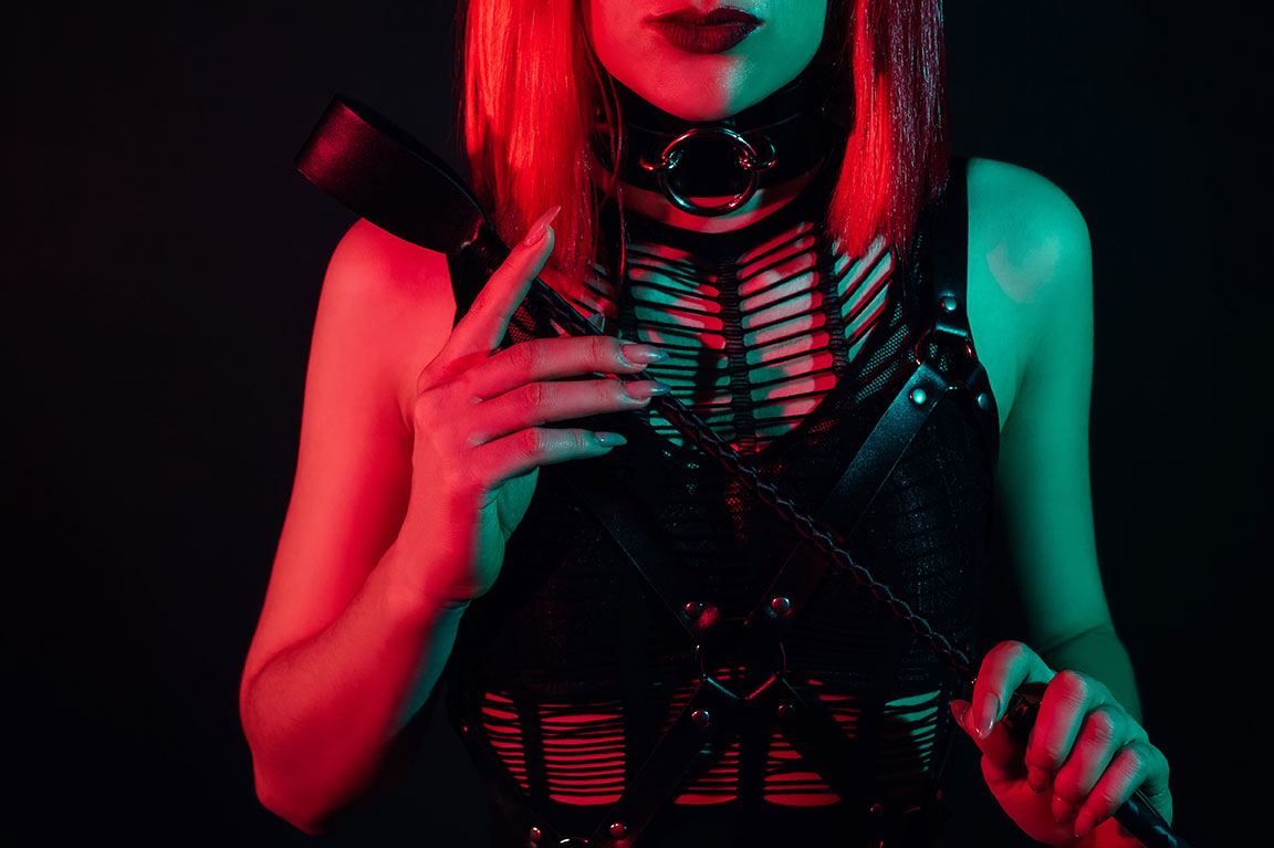 Frau in BDSM Outfit hält eine Lederpeitsche